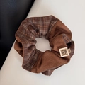 Detalle de un coletero tipo scrunchie de cuadros marrones con una etiqueta tejida - Maillard Marrón Café - Coletero Bicolor