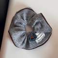 Detail eines grauen Strick-Haargummis mit Leopardenrand und besticktem Textetikett - Grauer Strickblumen-Scrunchie
