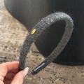 Detail eines dunkelgrauen Strick-Stirnbandes mit goldener Love-Plakette und Weblabel - Dunkelgrau