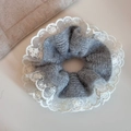 Close-up of grey knitted oversized scrunchie with delicate white lace embroidery trim - Knitted Lace Trim (FQ881036) / Gray