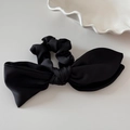 Detail of premium black satin bow hair scrunchie with smooth texture on a minimalist surface - Black