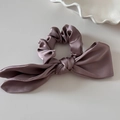 Detailed view of dusty pink satin silk hair scrunchie with long ribbon bow on white tray - Khaki