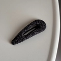 Detailed close-up of dark grey tweed woven hair clip on a textured beige surface - Teardrop Knitted BB Clip / Black