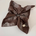 Detailed view of dark brown paisley print scrunchie with botanical logo charm - Coffee Square Style