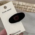 Close-up of velvet oval hair clip with cute brown bear head on textured card display - Black