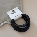 Macro detail of two black satin scrunchies with glossy texture on luxury card packaging - Dark Gray
