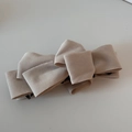 Detailed close-up of a beige multi-layered faux suede bow banana hair clip with a black fastener - Off White