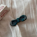 Détail d'une barrette nœud en acétate marbré avec strass sur un tissu en lin blanc - Vert