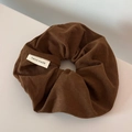 Macro shot of brown corduroy scrunchie fabric with a handmade white woven label detail - Brown