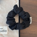 Détail d'un chouchou en tricot noir avec motif ajouré et étiquette de marque sur tissu - Petit Noir