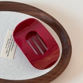 Detail von burgunderroter Retro-Haarklammer mit Goldlogo auf dunklem Holztablett-Hintergrund - Rot