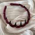 Detail of dark red knitted headband with black spike accents on soft linen fabric background - Red