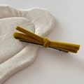 Detail of a mustard yellow velvet bow hair clip on a natural linen textured fabric - Yellow
