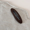 Gros plan d'une pince à cheveux ovale en similicuir marron sur tissu beige - Café Élégant - Barrette Ovale