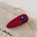 Detailed macro view of a red drop-shaped acetate hair clip with a blue floral decoration - Red