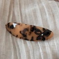 Detail view of tortoiseshell barrette with a black bow and crystal on beige linen - Tortoiseshell