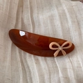 Detail of tortoiseshell acetate barrette with pink bow and crystal accent on light fabric - Caramel