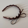 Detalle de diadema de cuero marrón con púas punk negras y lazo con amuleto dorado elegante - Diadema Lazo Cuero Marrón