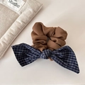 Detail eines braunen Baumwoll-Scrunchies mit dunkelblauer Karoschleife auf neutralem Grund - Hellkaffee Blau Kariert