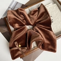 Detail of a large brown velvet bow scrunchie with a gold sphere on a wood tray - Brown
