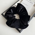 Close-up of black velvet ruffled hair scrunchie with logo tag on a jewelry tray - Black