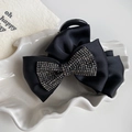 Dettaglio molletta per capelli in raso nero con strass scintillanti su vassoio bianco - Stile Fiocco con Strass