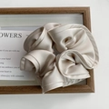 Detail of elegant champagne satin hair scrunchie with soft ruffles on a minimalist background - Off-white