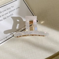Detail view of pearlescent white acetate hair claw with golden spring on textured background - T-Shape