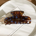 Detail of tortoiseshell acetate hair claw clip with golden logo on white tray - Blue Coffee