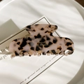 Detail of tortoise shell acetate hair claw with gold logo on an elegant display card - Light Leopard