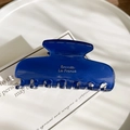 Dettaglio della molletta per capelli blu scuro con scritte dorate su un vassoio bianco - Blu Olografico