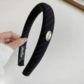 Detailed macro view of black striped fabric headband with oval gold metal logo - Black