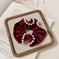 Dettaglio scrunchie in velluto bordeaux con perle decorative su un vassoio legno - Stile Bordo Perla
