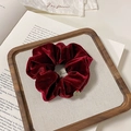 Dettaglio dell'elastico scrunchie in velluto rosso scuro con ciondolo dorato su vassoio - Stile Etichetta Dorata