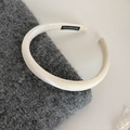 Detail of a creamy white padded satin headband with handmade label and glossy finish - White
