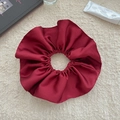 Close-up of a large burgundy satin scrunchie with soft folds on a plush background - Red