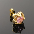 Détail d'une boucle d'oreille cœur dorée avec zircon rose sur une surface noire réfléchie - Or Zircon Rose