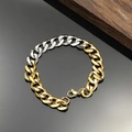 Detail eines zweifarbigen Gold- und Silber-Panzerarmbands mit Karabiner auf dunklem Holz - Gold & Silber