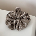 Close-up of champagne satin scrunchie with white polka dots and fashion textile label - Brown