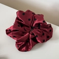 Gros plan sur un chouchou en satin rouge foncé à gros pois noirs et plis élégants - Rouge