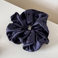 Détail d'un chouchou en satin bleu marine à pois noirs avec une texture de tissu lisse - Bleu marine