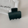 Detail of dark green resin hair claw clip with glossy finish on a beige fabric background - Green