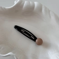 Detail of a black metal snap hair clip with a light coffee bead decoration on shell dish - Black