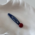 Detail of royal blue metal BB clip with red resin bead on a white shell plate - Blue
