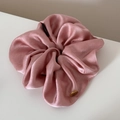 Detalle de un coletero de satén rosa con un dije metálico dorado de marca propia - Scrunchie / Coletero Rosa Etiqueta Dorada