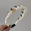 Detalle de coletero de satén crema trenzado con puntas negras y etiqueta metálica - Diadema Blanco Crema Etiqueta Dorada