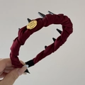 Primer plano de coletero de satén burdeos con puntas negras y placa de metal dorado - Diadema Rojo Etiqueta Dorada