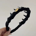 Detalle de una diadema plisada negra con pinchos grises y una placa de logotipo dorada - Diadema Negro Etiqueta Dorada