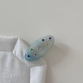 Dettaglio di fermaglio ovale in acetato con strass colorati su superficie di lino - Blu