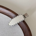 Dettaglio molletta per capelli crema con cuciture nere su vassoio in legno - Stile Ellisse Tratteggiato (FJ892858) / Clip Bianca Tratteggiata